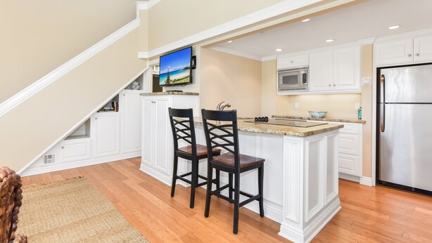 A kitchen with white cabinetry, a stainless steel refrigerator, and a built-in island with two bar stools.