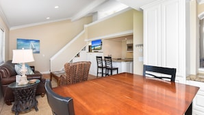A spacious living area with a wooden dining table, comfortable seating, a staircase leading to an upper level, and a kitchen area.
