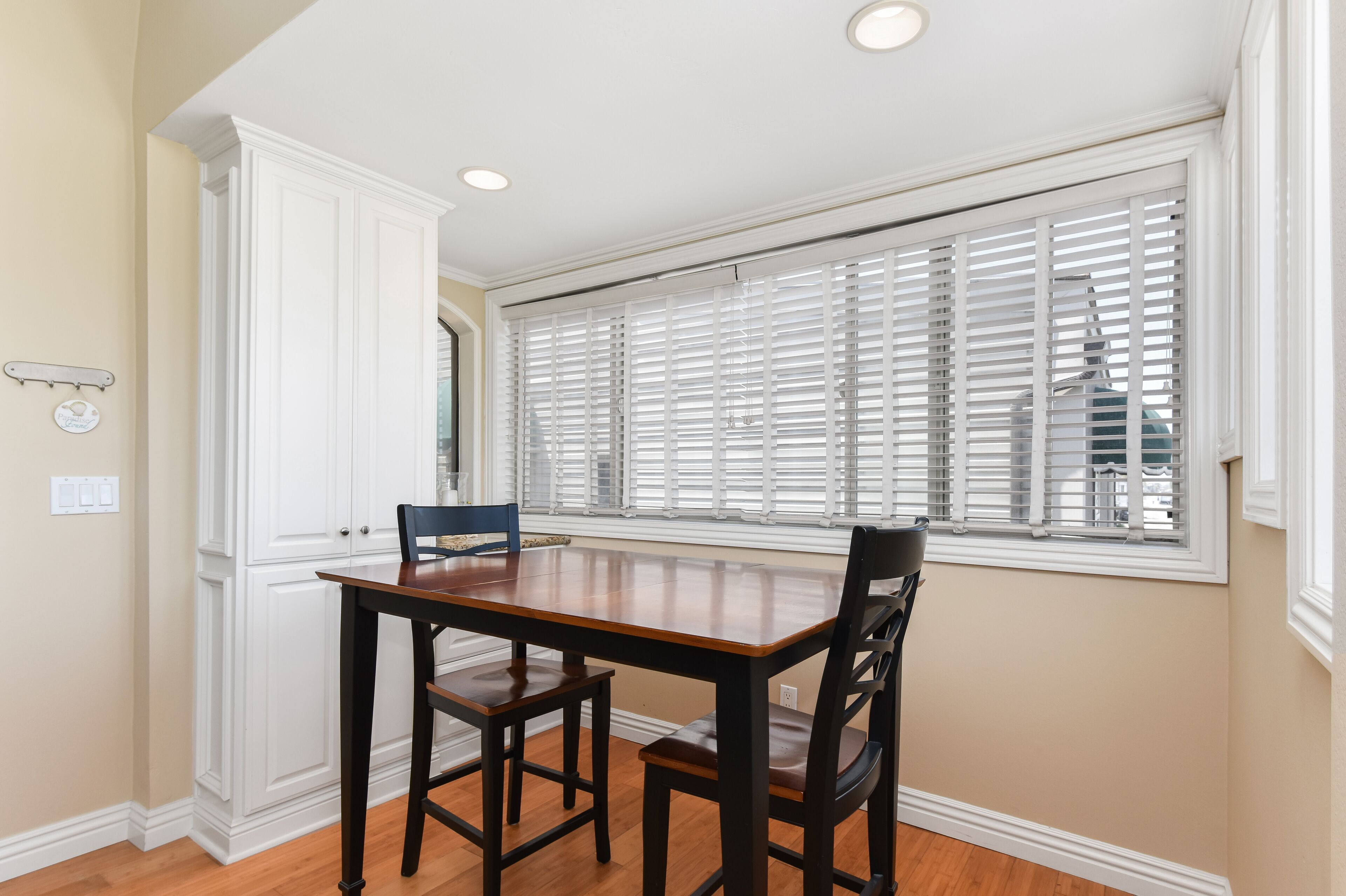 A dining area with a wooden table and chairs, a window with blinds, and a white cabinet.