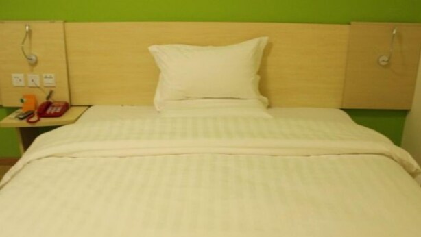 Una cama con cabecera, almohada y mesita de noche con un teléfono.