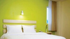 Una habitación de hotel con una cama, una mesita de noche y un ventanal con cortinas.