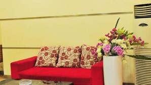 Un sofá rojo con almohadones estampados, un jarrón blanco con flores y un diseño de pared a rayas.