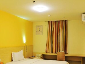 Habitació d'hotel amb llit, escriptori, cadira, tauleta de nit, làmpada, finestra amb cortines i rellotge de paret.