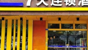 Entrada de un hotel con un cartel que indica '7 días' y un elemento decorativo vertical amarillo y azul.