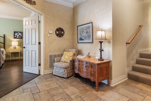 Un couloir avec une chaise, une table d’appoint en bois, une lampe, un tableau encadré et un escalier.