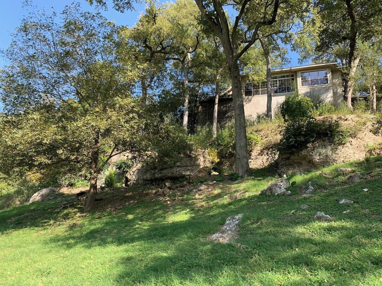 A house with a sloped roof, surrounded by trees and a grassy area.