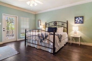 Une chambre à coucher avec un lit en métal, une table de chevet avec une lampe, une porte donnant sur une vue agréable et une fenêtre avec des stores.