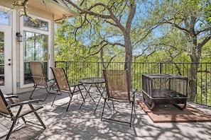 Une terrasse extérieure couverte, dotée de chaises et d’un barbecue, et entourée d’arbres.