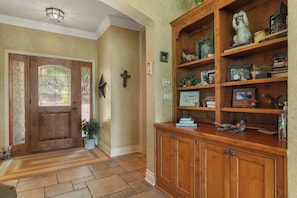 Une porte en bois ornée d’un vitrail, un meuble en bois avec des étagères et un crucifix fixé au mur.