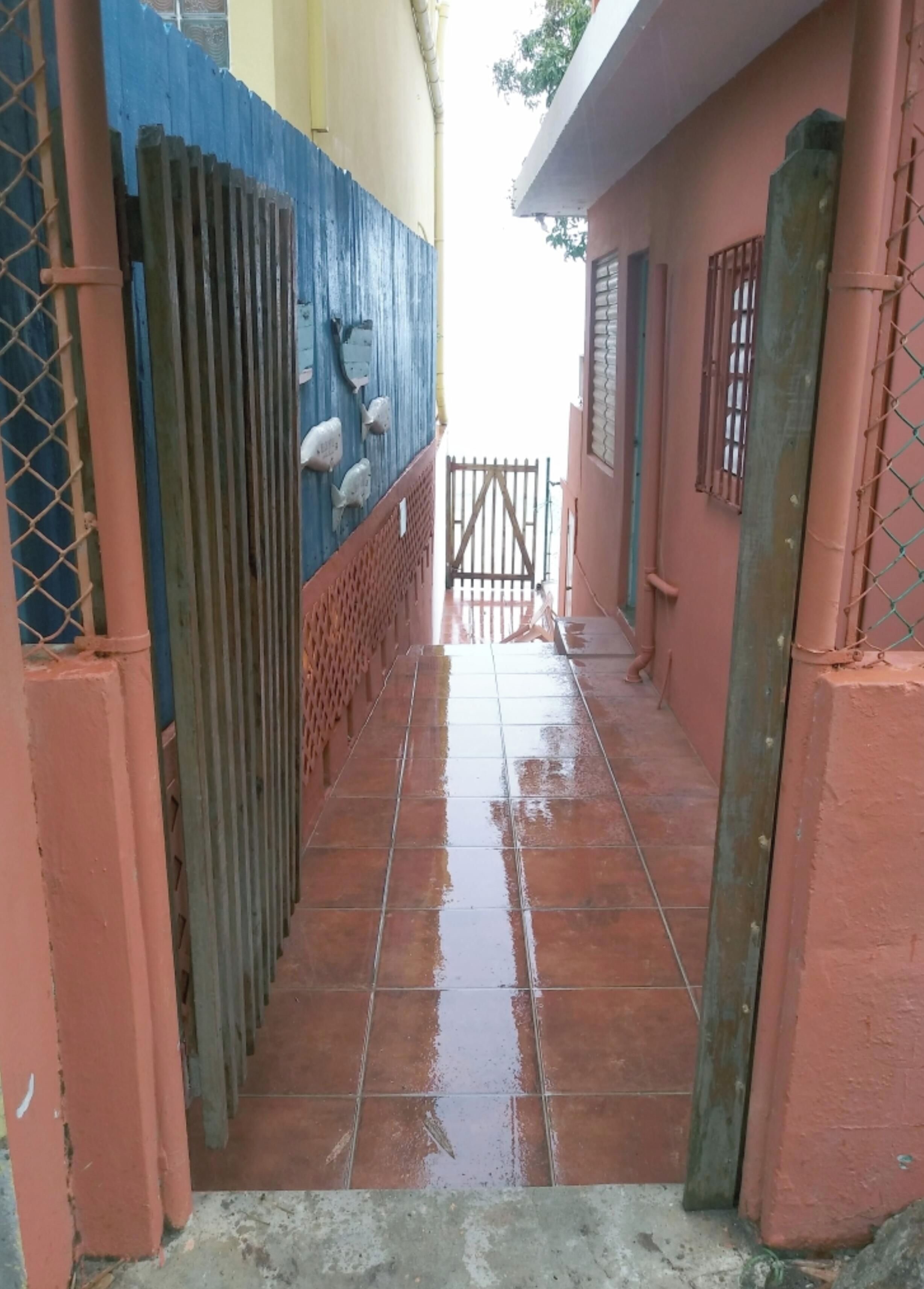 A narrow corridor with a tiled floor, a metal gate, and a blue fence on one side.