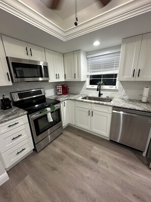 A modern kitchen with white cabinets, stainless steel appliances, a marble countertop, and a wooden floor.