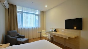Ein Hotelzimmer mit Bett, Schreibtisch, Sessel, Fernseher und einem fensterbepflanzten Fenster.