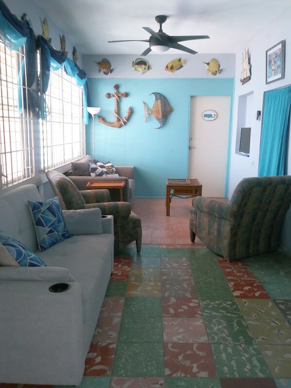 Un salon avec un mur bleu, un ventilateur de plafond et une décoration murale sur le thème des poissons.