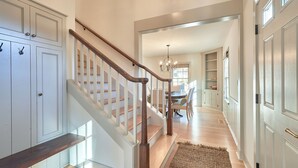 A staircase with wooden handrails and white walls, leading to a dining area with a chandelier. - Luxe remodel, three King ensuites, walk to 3rd St (McMinnville)