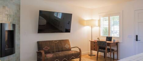 Una habitación acogedora con sofá, escritorio con silla, televisor montado en la pared y ventana con luz natural.