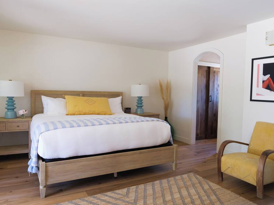A bedroom with a wooden bed, two bedside tables with lamps, a chair, and a framed picture on the wall.