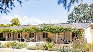 A building with a stone facade, multiple windows, and a covered patio area with a hammock. - Hotel Ynez (Solvang)