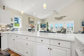 Uma cozinha moderna com armários brancos, uma ilha grande e luminárias pendentes.