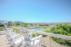Une terrasse dotée de chaises blanches, donnant sur une piscine et offrant une vue pittoresque sur un pont et la verdure environnante.