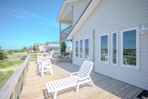 Um deck de madeira com espreguiçadeiras brancas e uma mesa, com vista para a praia.