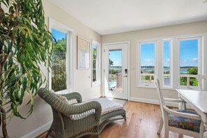 Quarto com cadeira de vime, uma mesinha e vista para o exterior, com porta que dá para fora.