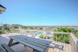 Una terraza de madera con sillas Adirondack y una mesa de picnic, con vistas a un cuerpo de agua y follaje.