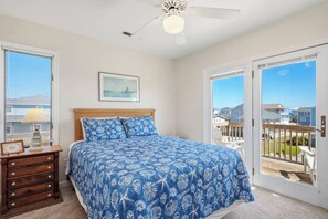 Un dormitorio con cama, cómoda, ventilador de techo, ventana y puerta que da a un balcón.