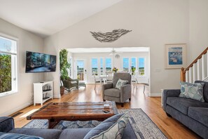 A spacious living room with a wooden coffee table, grey sofa, and a television mounted on the wall. - Sound Bite: Ocean View Home with Dock on Eastern Channel! (Oak Island)
