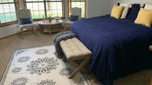 Een slaapkamer met een groot bed, twee stoelen, een ronde tafel en een decoratief vloerkleed.