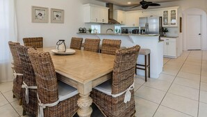 Een moderne keuken met witte kastjes, een centraal eiland en een eethoek met rieten stoelen.