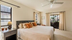 Ein Schlafzimmer mit einem großen Bett, einem Nachttisch mit Lampe, einem Deckenventilator und Blick ins Freie durch ein Fenster.