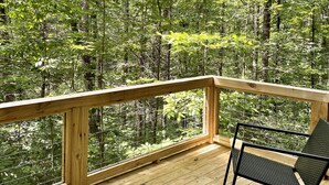 Eine Holzterrasse mit Glasgeländer, das auf einen Wald blickt.