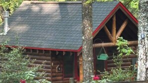 Eine rustikale Holzhütte mit rotem Dach und Schornstein, umgeben von üppigem Grün und blühenden Pflanzen.