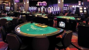 Ein Casino mit mehreren Blackjack-Tischen, Stühlen und Spielautomaten.