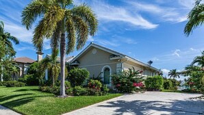 A single-story house with a beige facade, a front lawn, and palm trees.