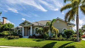 A two-story house with a symmetrical facade, a central entrance with a covered porch, and a well-maintained lawn with palm trees.
