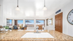 A kitchen with a granite countertop, wooden cabinets, and a view of the beach through large windows. - 2 Bed Oceanfront w/ patio on the Sand in Quiet West Newport (Newport Beach)