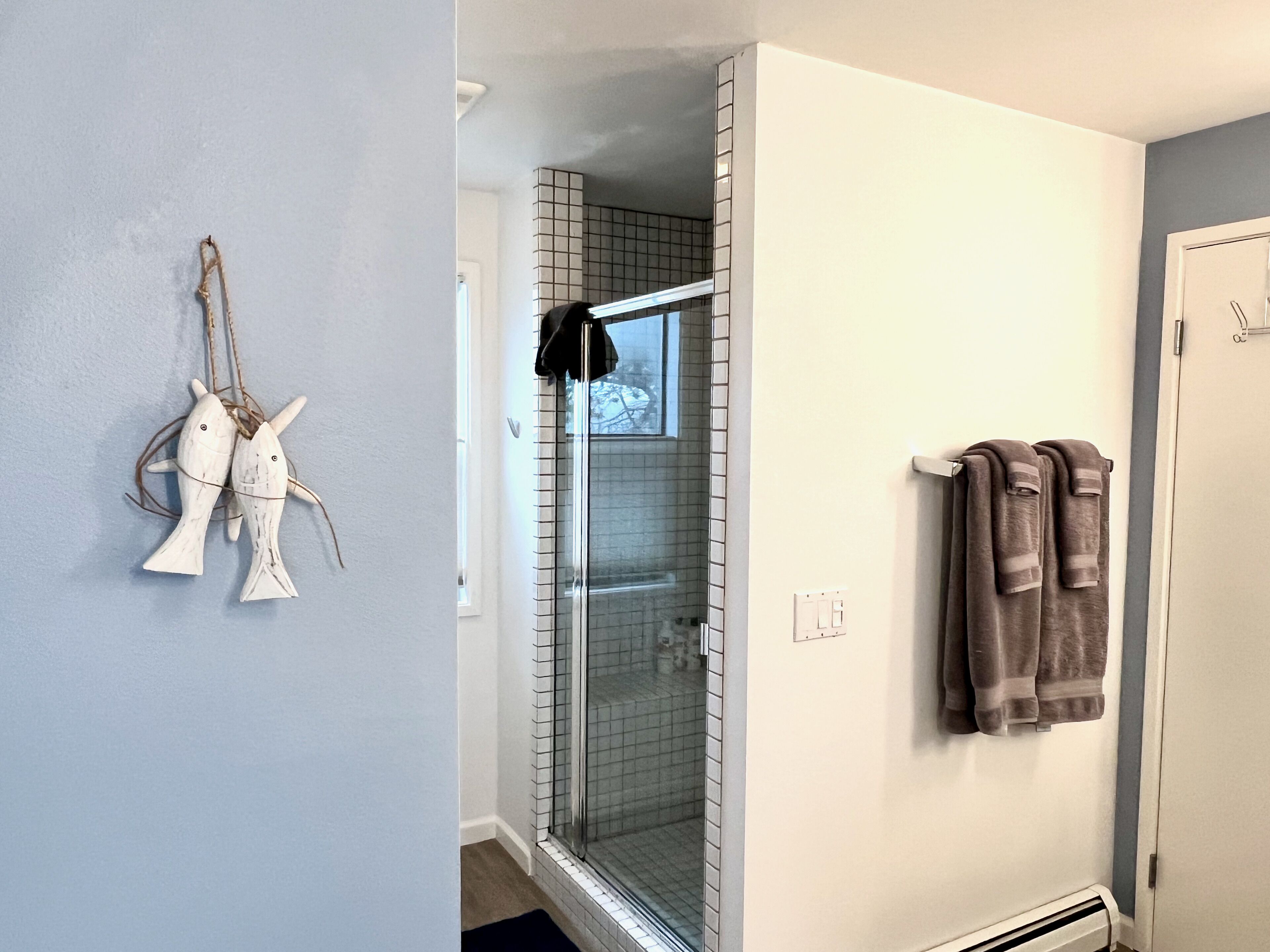 A bathroom with a glass shower door, a towel rack with towels, and a wall-mounted fish decoration.