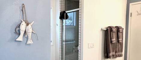 A bathroom with a glass shower door, a towel rack with towels, and a wall-mounted fish decoration.