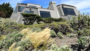 A modern house with a sloped roof, large windows, and a well-maintained garden with various plants and shrubs. - Dazzling Luxury Ocean views, Hot Tub, Golf, AC, Theater, Chef Options @SwitiHoso (Bodega Bay)