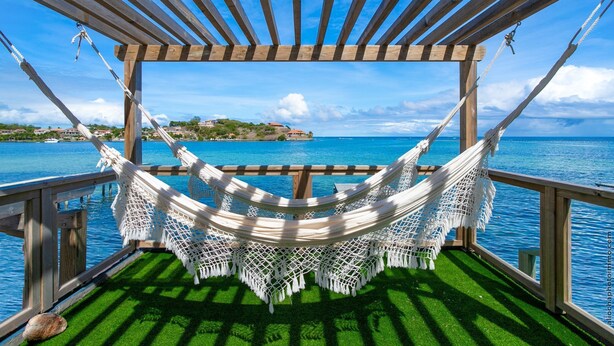 Een hangmat onder een houten pergola met uitzicht op de oceaan en een eiland in de verte.