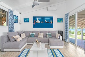 Een moderne woonkamer met een grijze modulaire bank, een witte salontafel en een groot blauw kunstwerk met zeilboten.