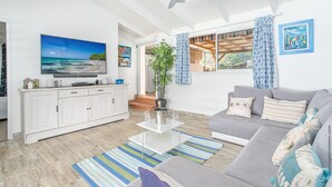 Een woonkamer met een grijze bank, een salontafel, een televisie en een plafondventilator.