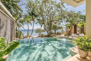 A pool area with clear water, surrounded by tropical plants and trees, overlooking a beach. - Lola by Coco B Isla (Isla Mujeres)