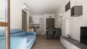 A modern living room with a sofa, a dining area, kitchen, and a TV.