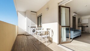 A balcony with a washing machine, a table with chairs, and a blue sofa.