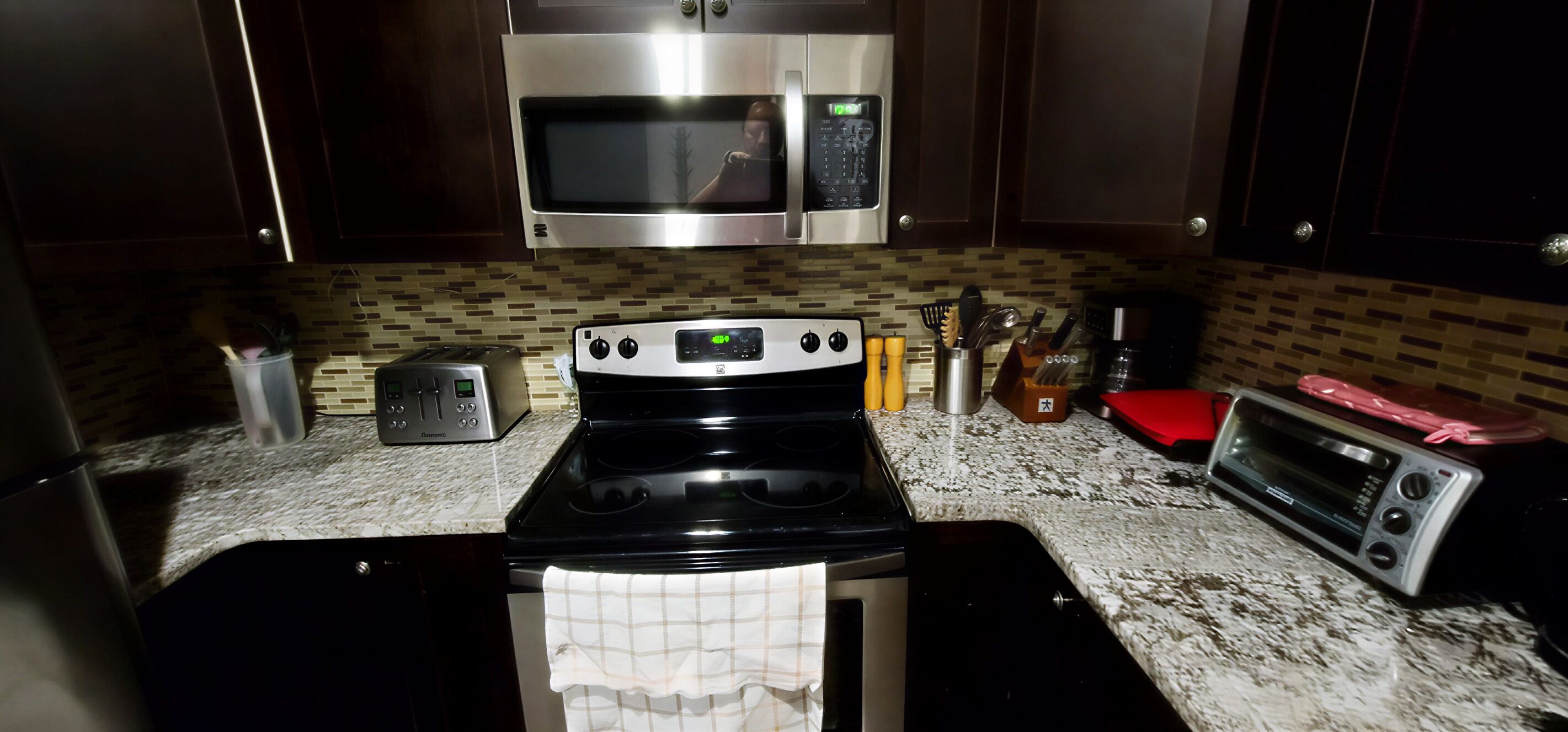 A kitchen with a microwave, toaster, stove, and a red cutting board.