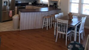 Une cuisine moderne dotée d’un îlot central, d’appareils électroménagers en acier inoxydable et d’un coin repas avec des chaises en bois.