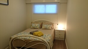 Un dormitorio pequeño y ordenado con cama, mesita de noche y ventana.