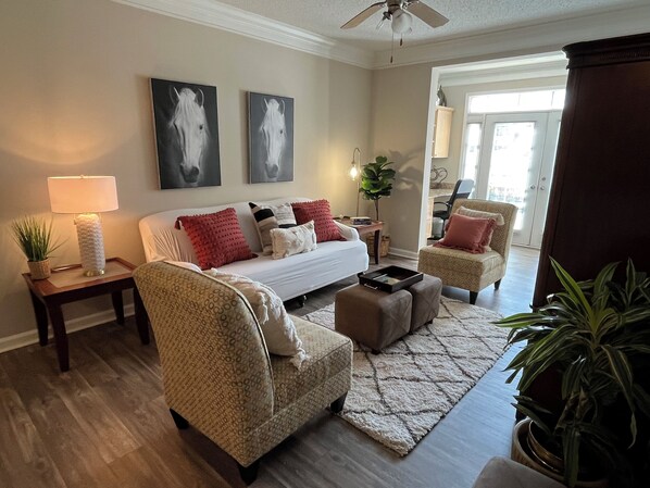 A living room with a sofa, two armchairs, a coffee table, a lamp, and two wall-mounted paintings. - Corporate Fully Furnished 2 br/2ba Apt with sunroom in Alpharetta (Alpharetta)